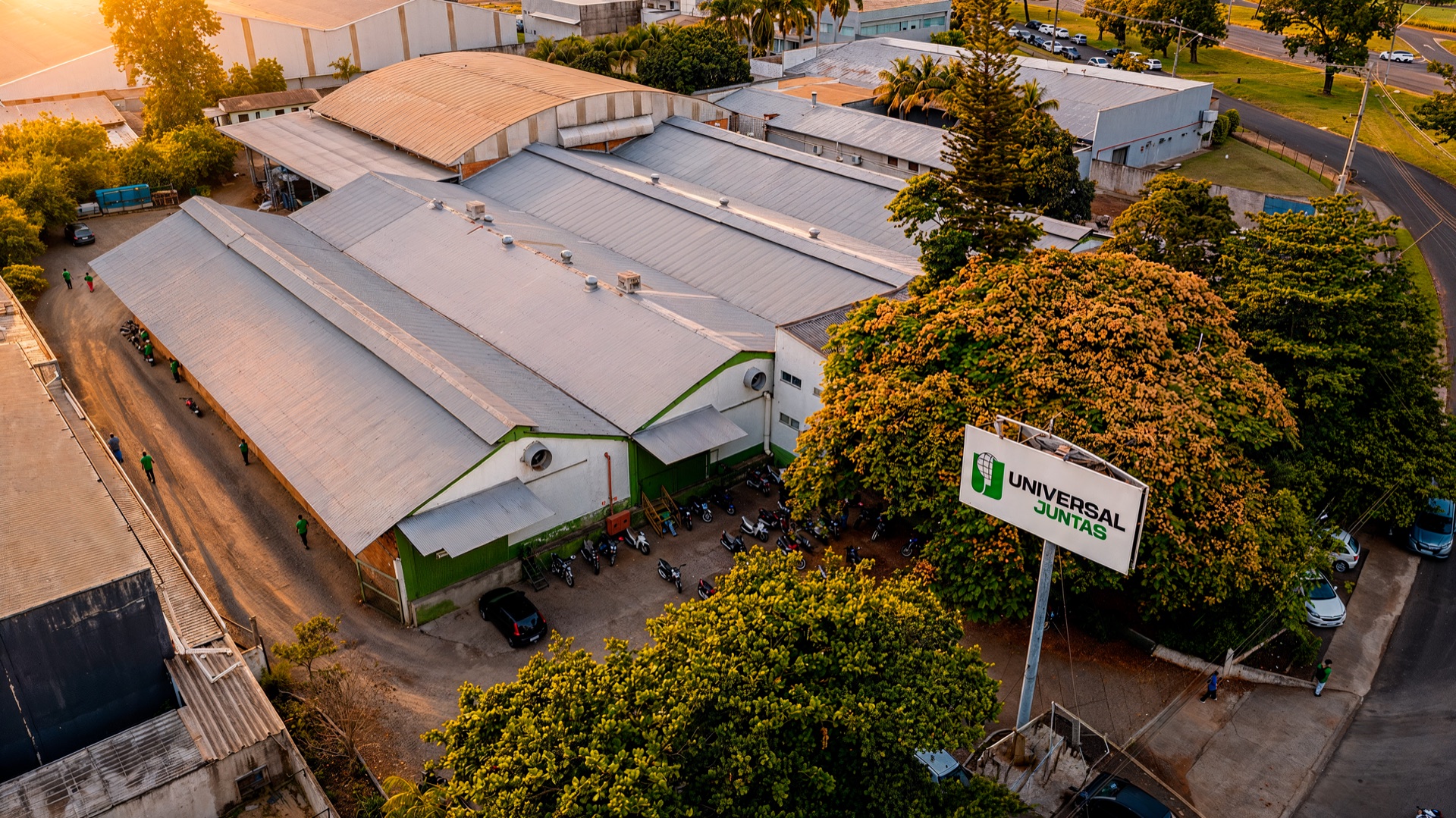 Vista aérea da unidade industrial da Universal Juntas ao entardecer, com a placa da empresa na entrada